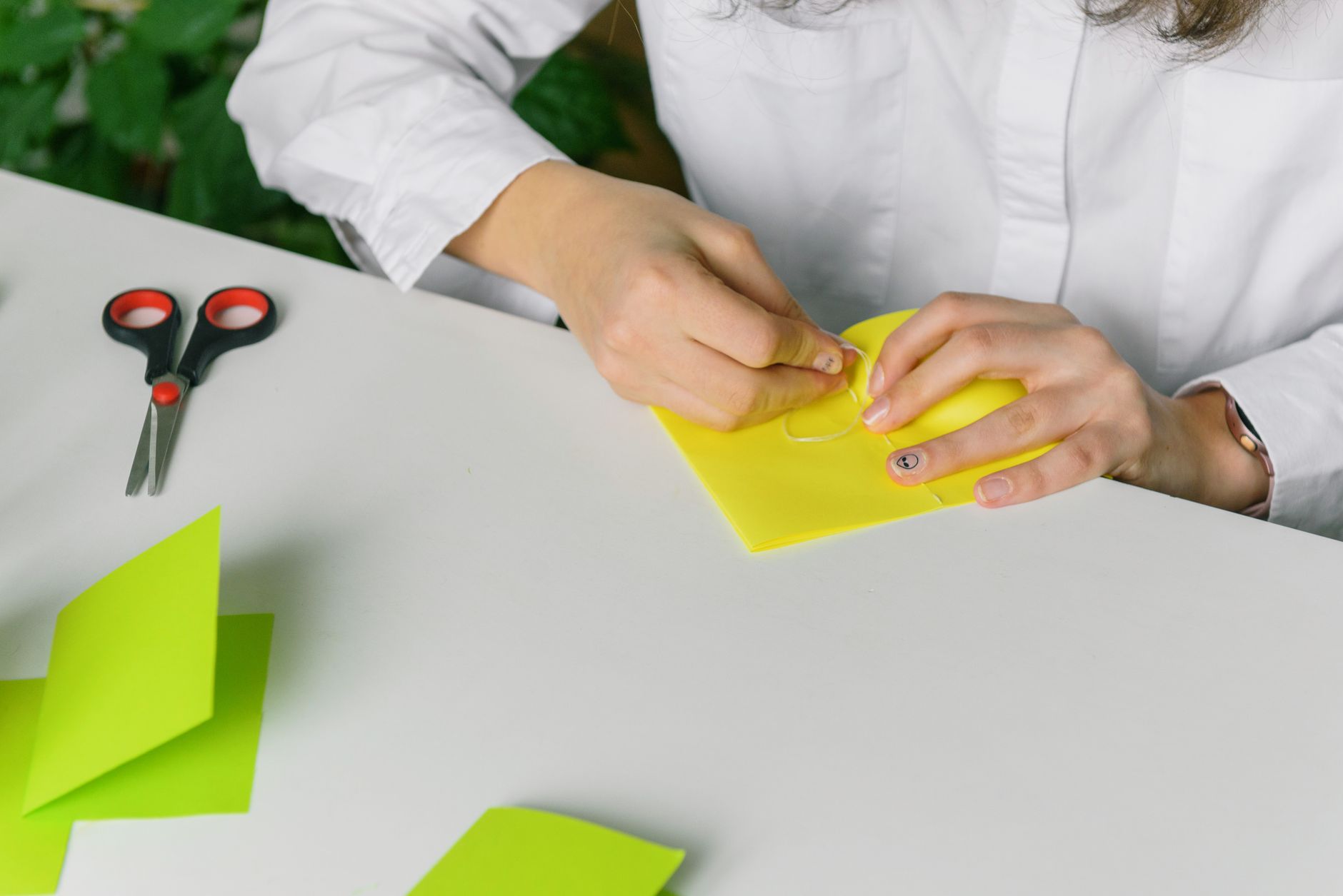Close-up of a woman crafting with yellow paper and tools like scissors on a desk.