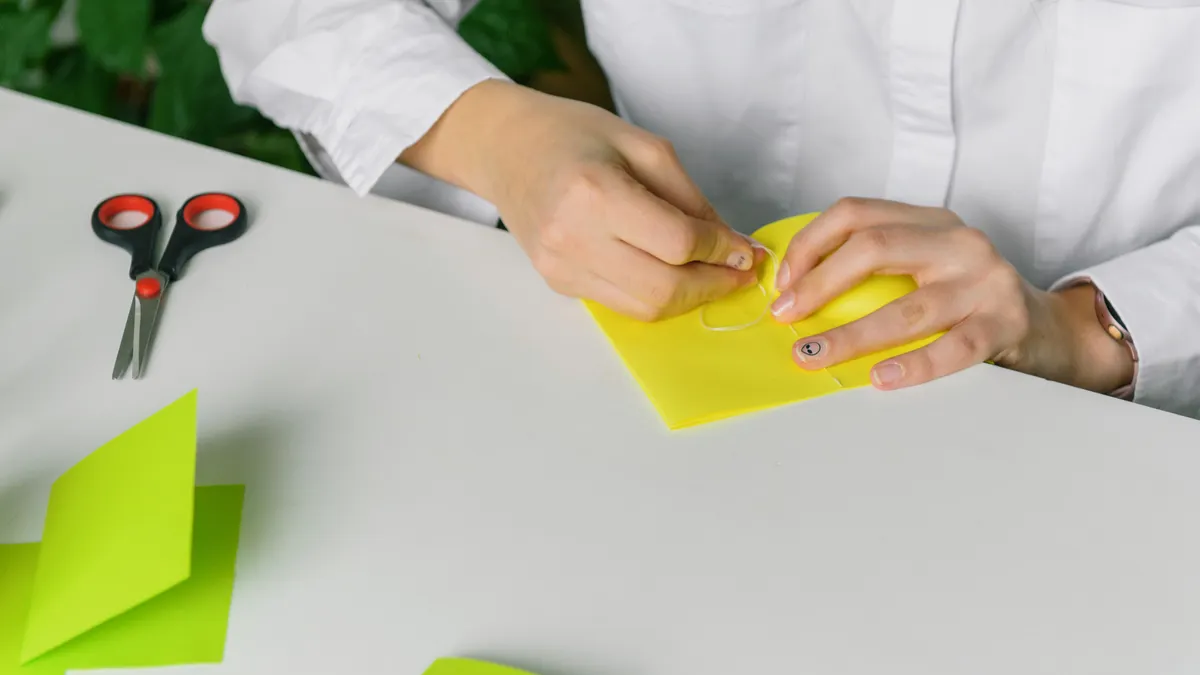 Origami for Beginners: Simple Paper Folds to Start With Hands folding yellow paper on a desk