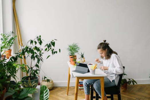 Woman sitting at desk in a cozy room, working on a tablet amidst various houseplants.