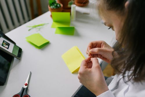 Free Woman threading a needle at a desk with colorful paper and craft supplies. Stock Photo