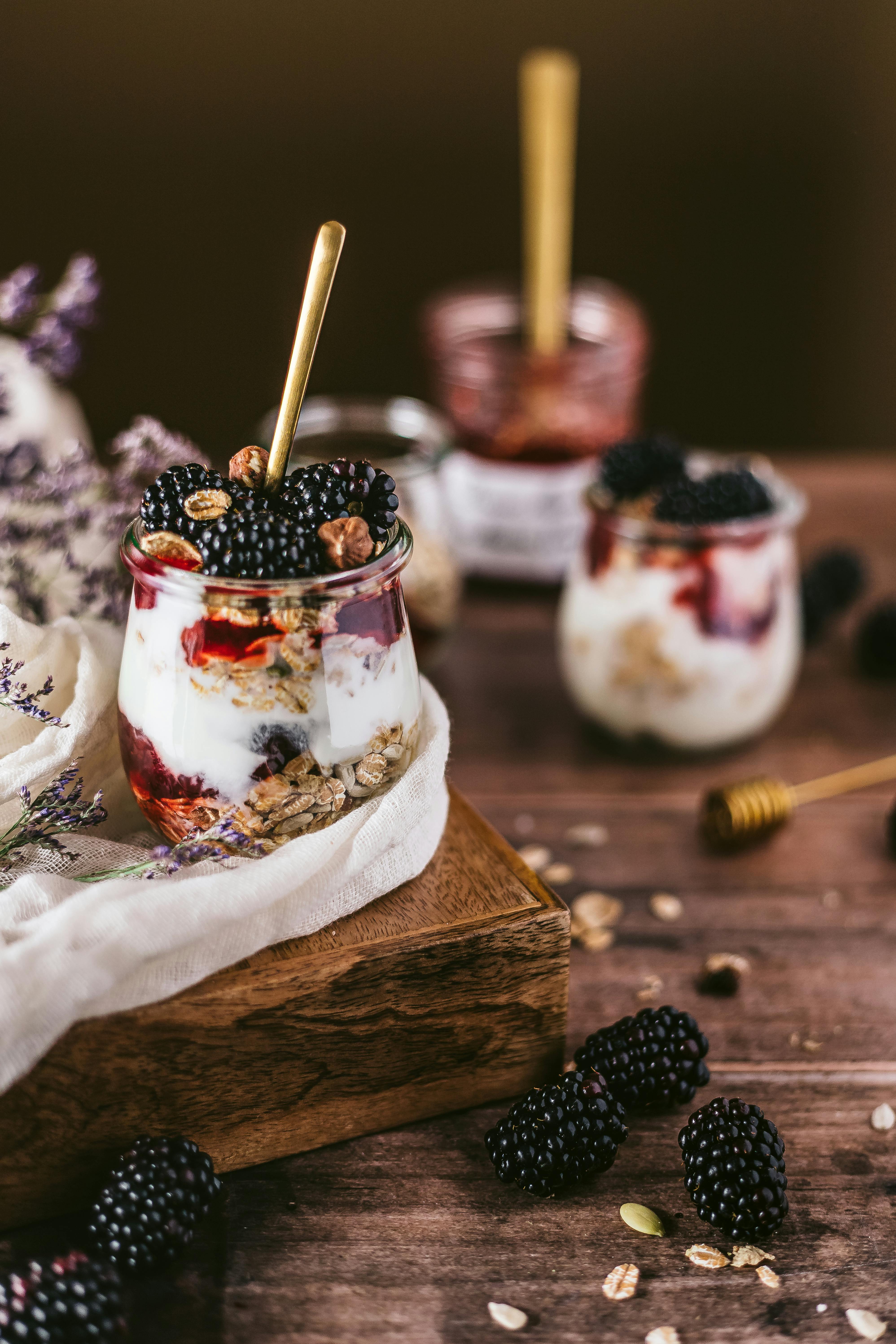 Tempting blackberry yogurt parfait in glass jars on wooden table, perfect for breakfast or dessert.