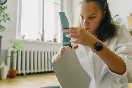 Free A young woman attentively cutting paper indoors, engaging in a creative craft project. Natural light setting. Stock Photo