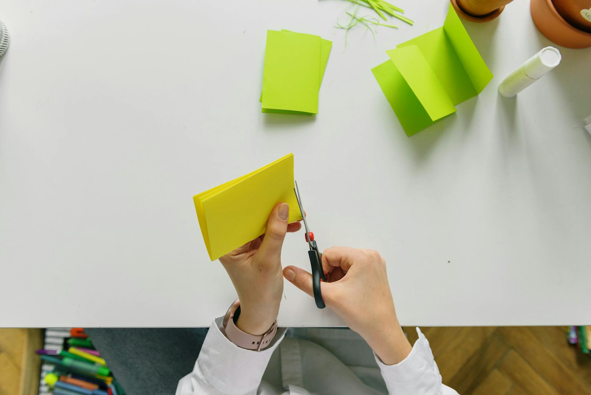 Hands using scissors to cut yellow paper, ideal for craft and school projects.