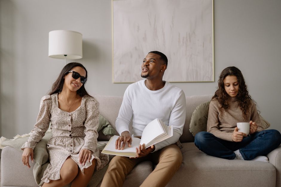 Three people enjoying a relaxed setting with a book and coffee in a living room environment.