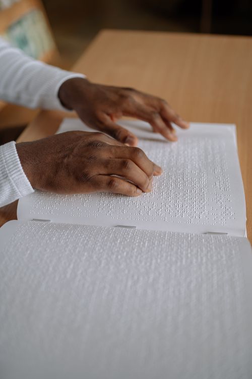 Free Close-up of hands reading a Braille book on a desk indoors, highlighting tactile reading. Stock Photo