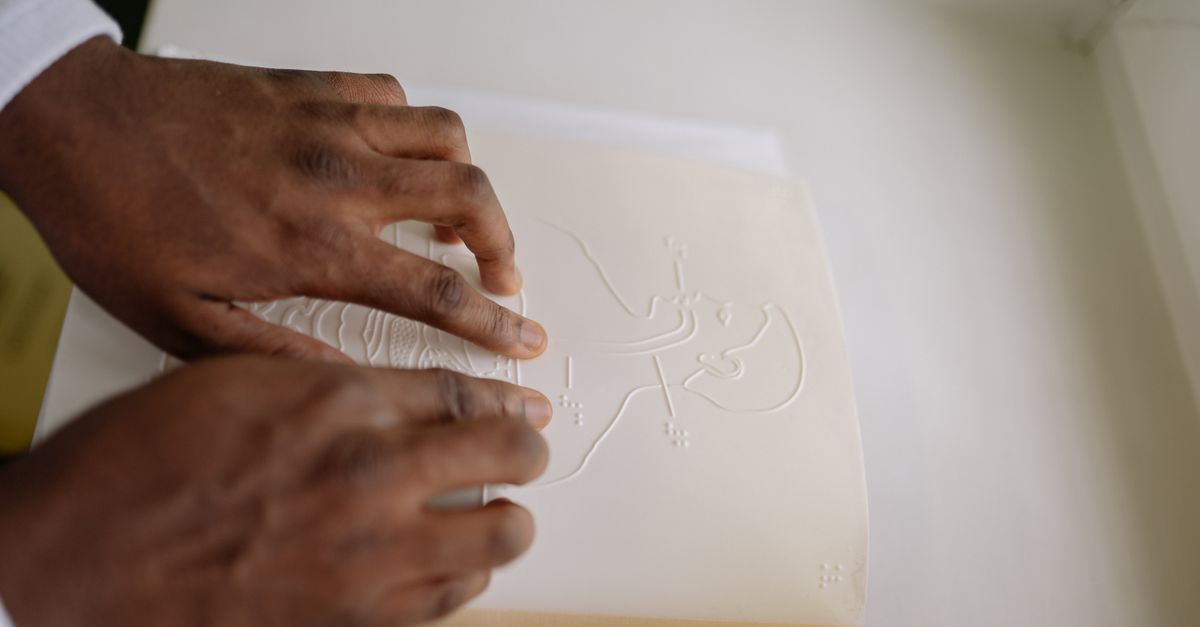Close-up of hands reading a tactile, braille-embossed educational book indoors.