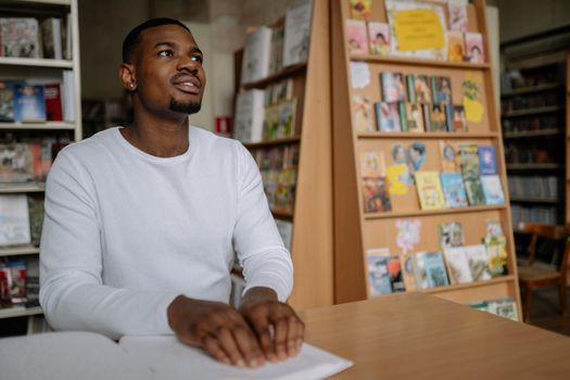A man with visual impairment happily reads Braille at a library desk.