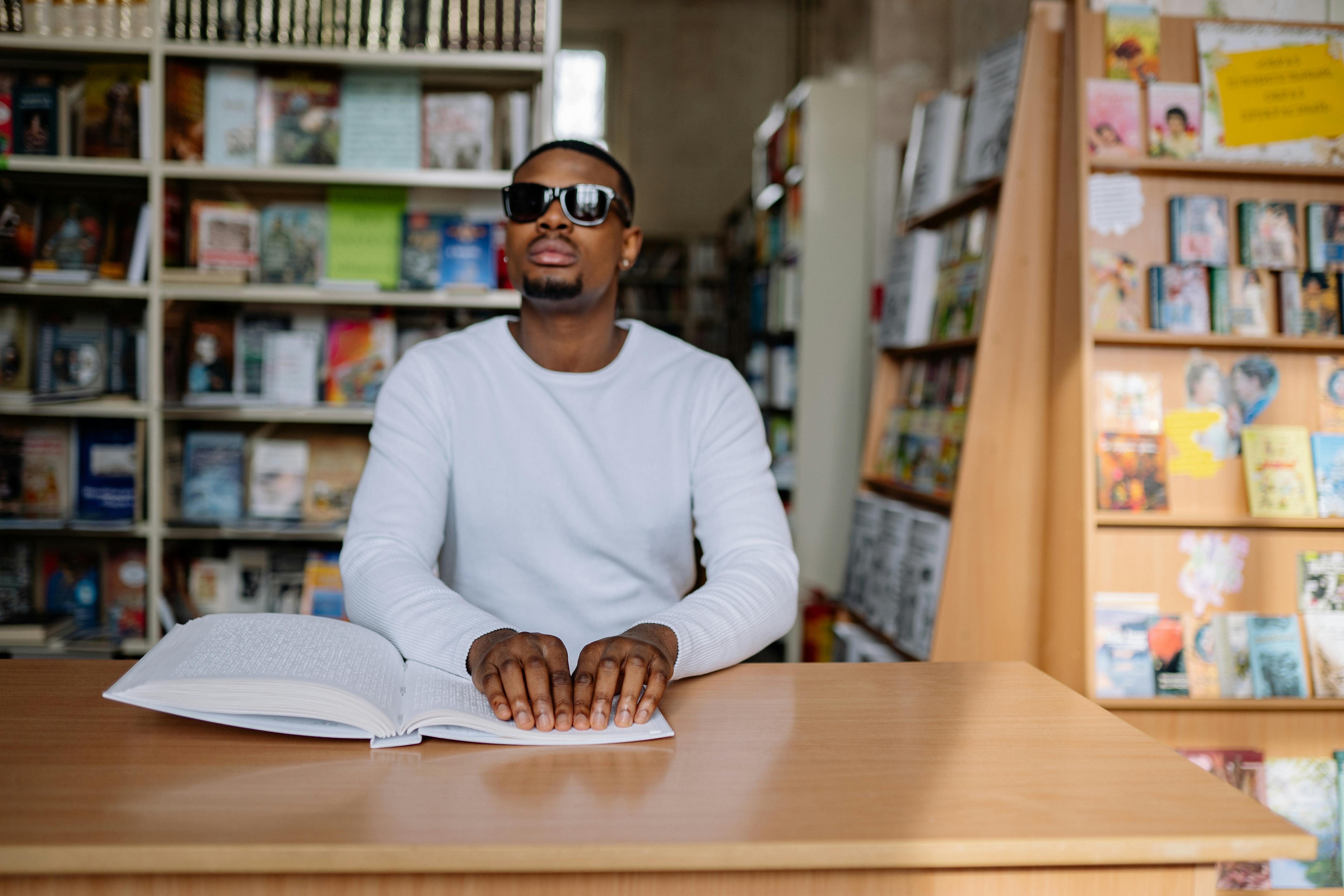 man in white sweater wearing black sunglasses reading braille