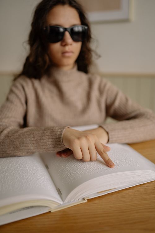 Free A woman wearing sunglasses reading a Braille book, emphasizing accessibility and education. Stock Photo