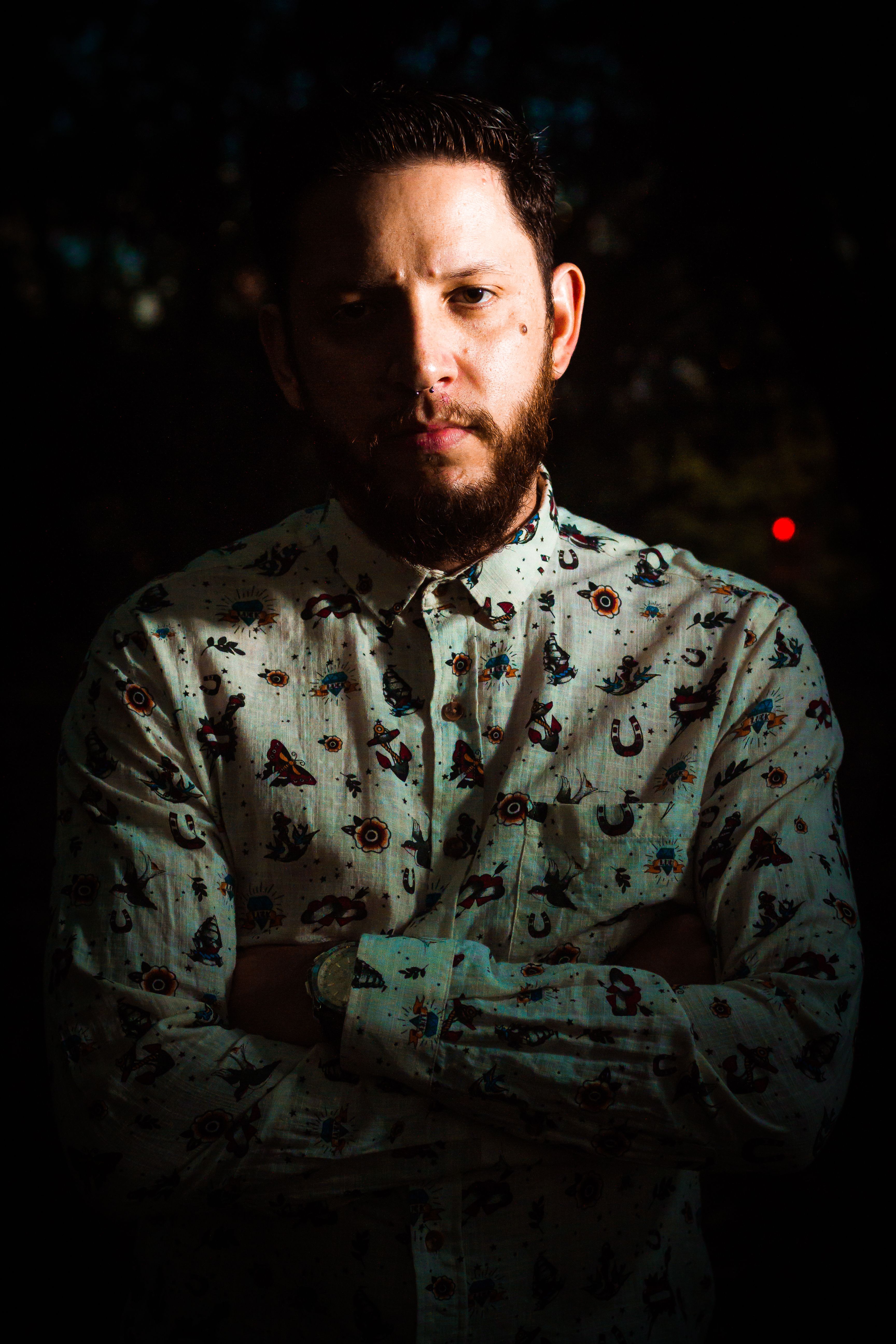 Close-up portrait of a man with a beard and printed shirt, captured with dramatic lighting.