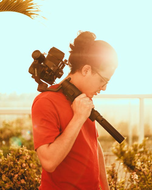 Pensive man with camera under blue sky near plants