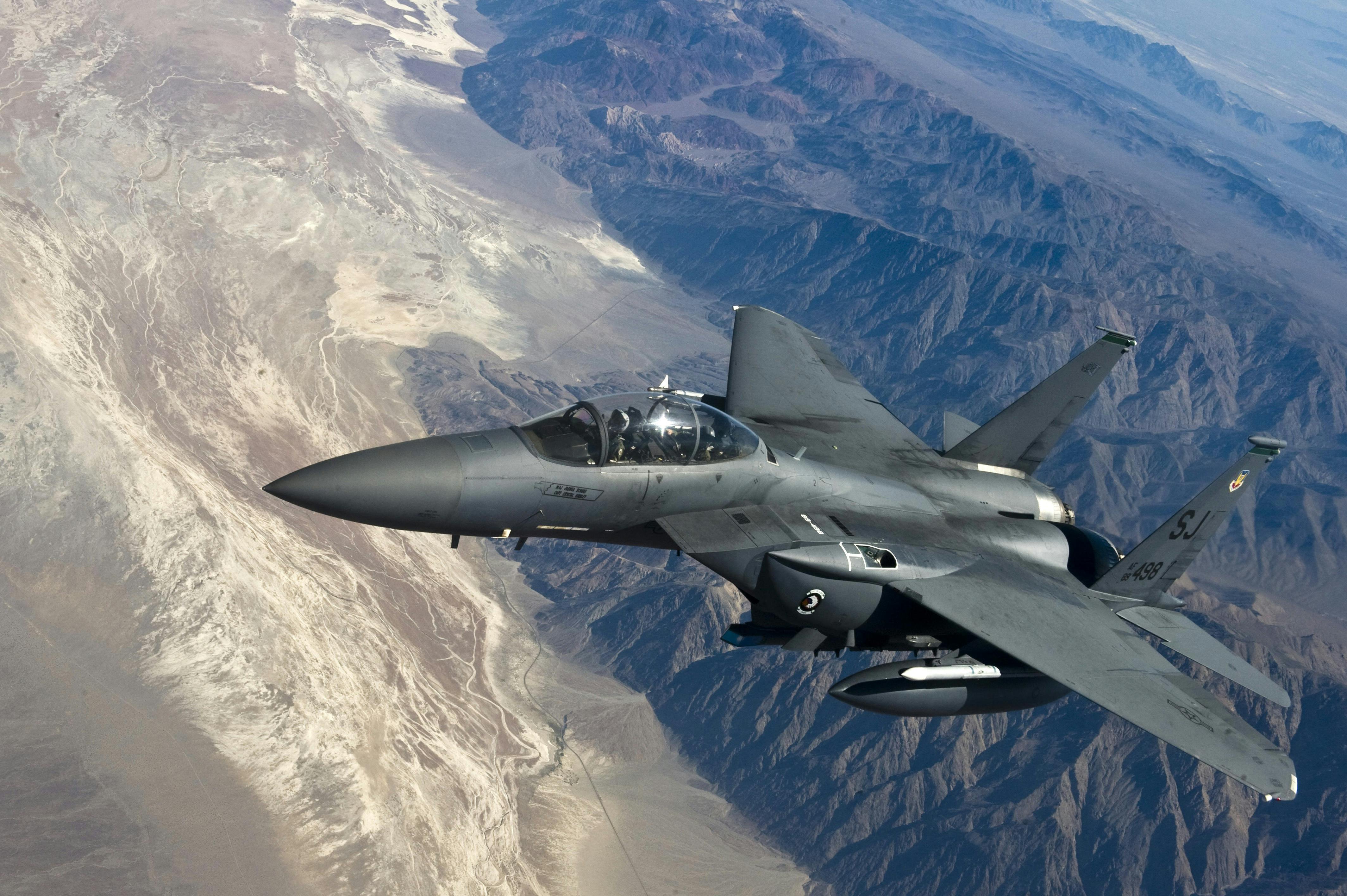 A modern fighter jet flying over mountainous terrain.