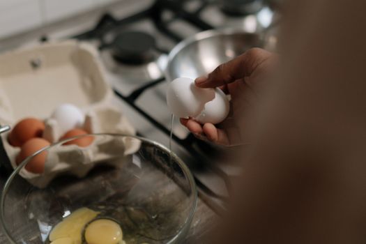 Hand cracks an egg into a glass bowl on a kitchen counter, perfect for cooking concepts.