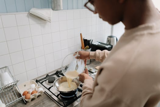 Man pouring egg mixture into a frying pan for an omelette in a modern kitchen.