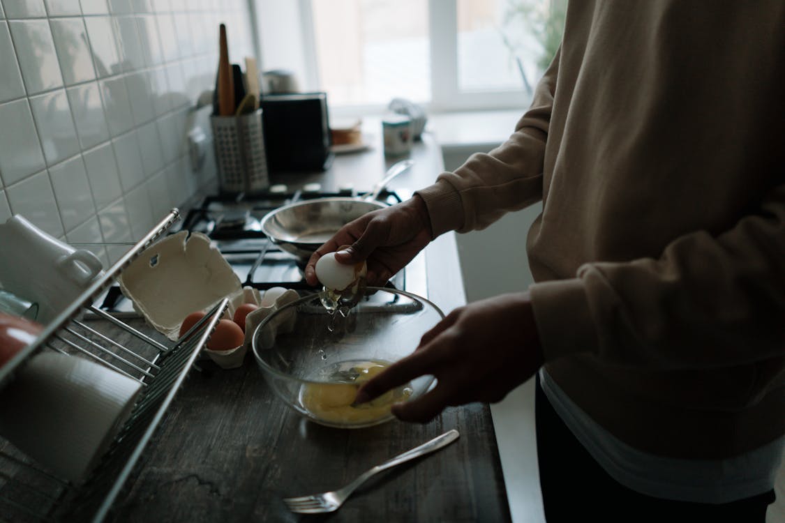 A person in Sweater Pouring Eggs into the Glass Bowl