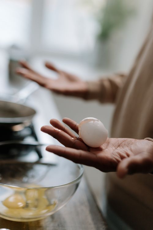 Free Hands carefully holding a broken egg over a bowl in a kitchen setting, showcasing cooking preparation. Stock Photo