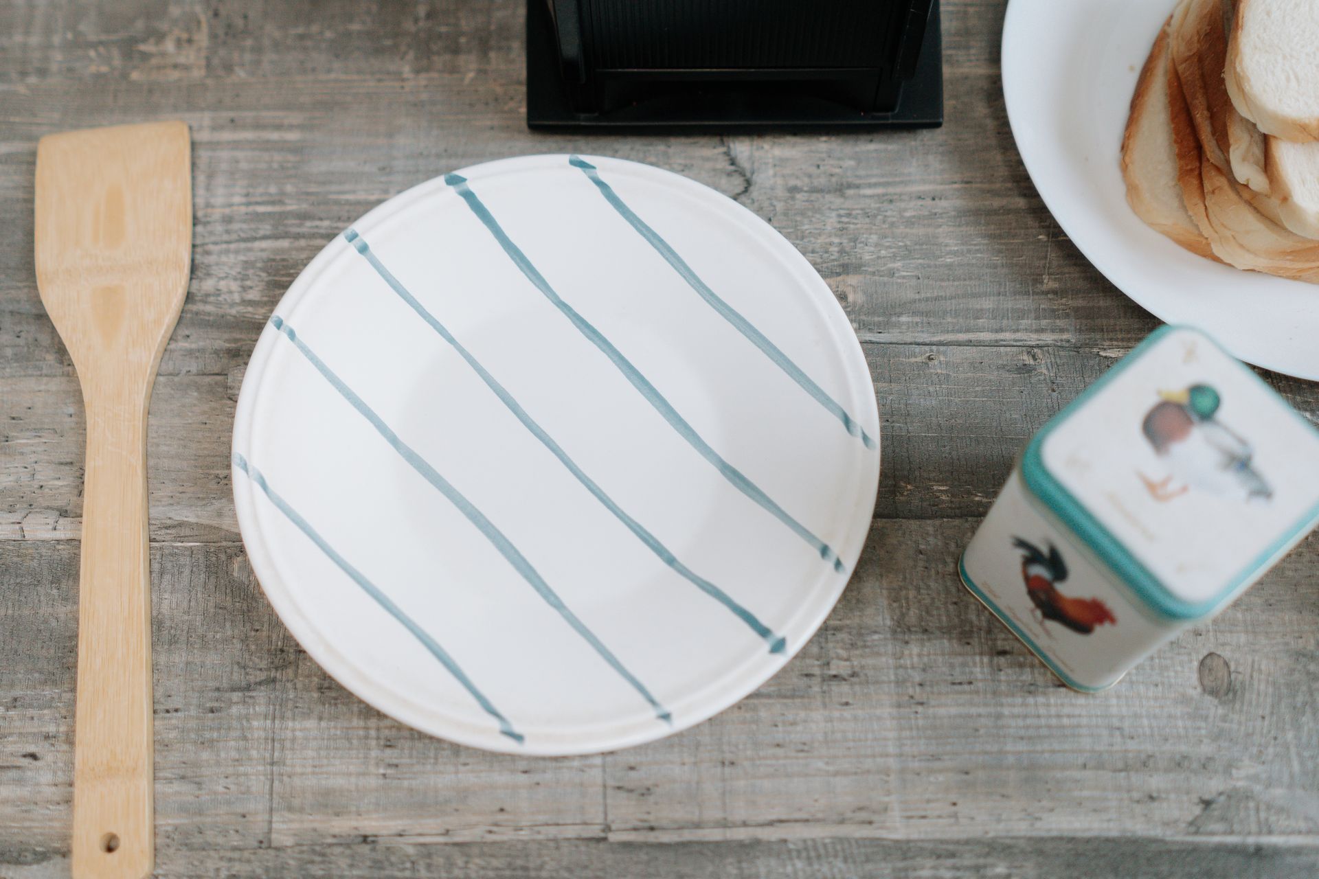 A rustic kitchen setup featuring a striped plate on a wooden surface, bread, and utensils.