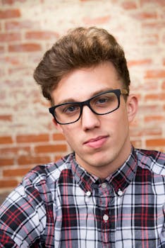 一个戴眼镜、穿格子衬衫的年轻人靠在砖墙上的肖像