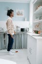 Woman in Pink Sweater and Blue Pants Standing in Front of Kitchen Sink