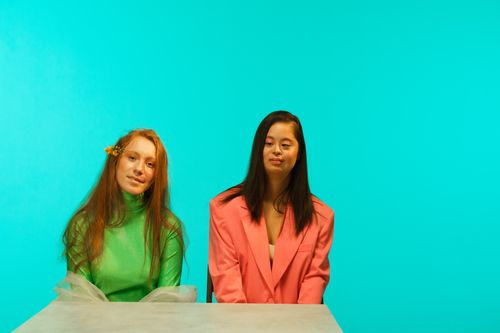 Free Two young women in colorful outfits with a vibrant turquoise background. Stock Photo
