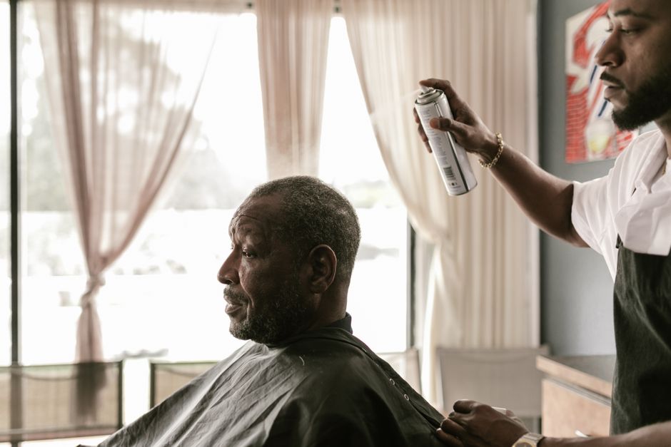 Homem recebendo um corte de cabelo em um cabeleireiro, com muita luz natural vindo das janelas ao fundo.