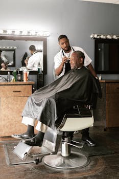 Barber attending to an elderly man in a modern barbershop setting.