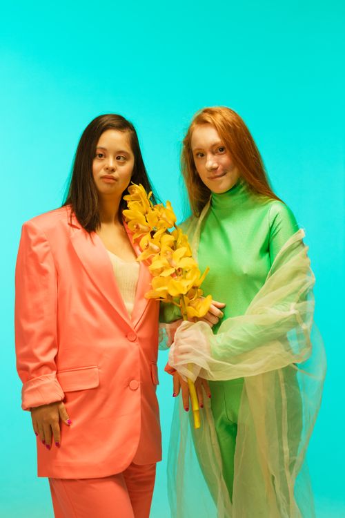 Free Two women pose with flowers against a vibrant teal background, showcasing fashion and diversity. Stock Photo