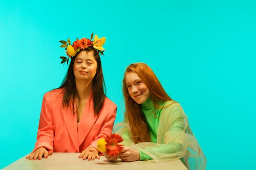 Women in Stylish Outfits Posing with Flowers while Sitting at a Table