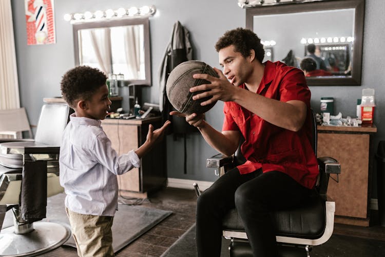 A Man In A Barber Chair Showing A Basketball To A Kic