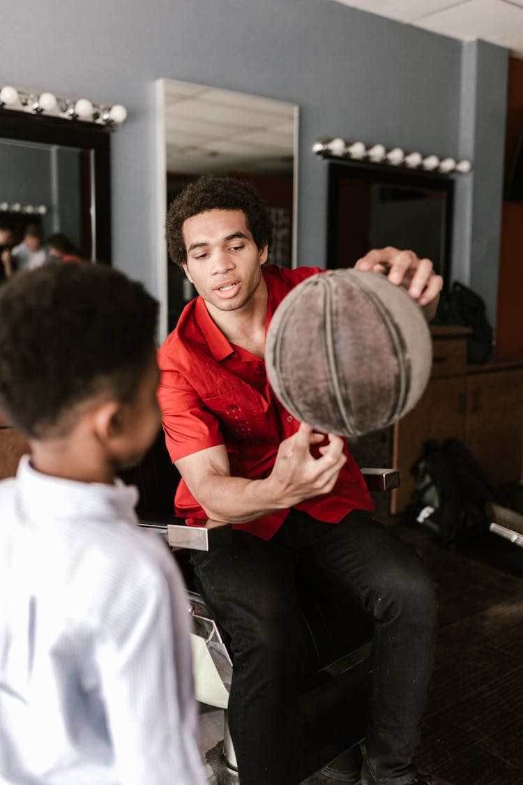 A Man In A Barber Chair Showing A Basketball To A Boy