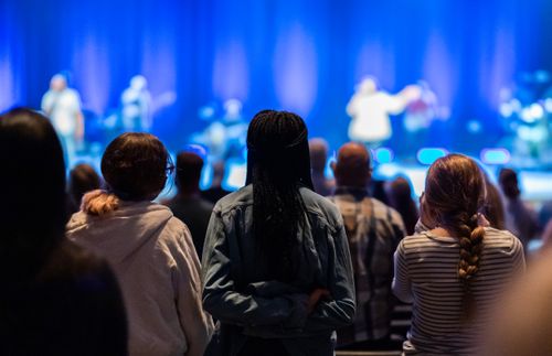 Free Back view of unrecognizable people looking at stage during performance in concert hall with shining lamps Stock Photo