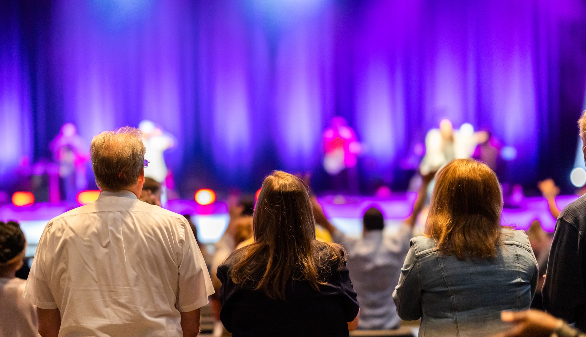 Back view of anonymous people looking at stage and listening to performance attentively