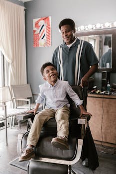 A smiling child sits in a barber chair, enjoying a haircut experience indoors.