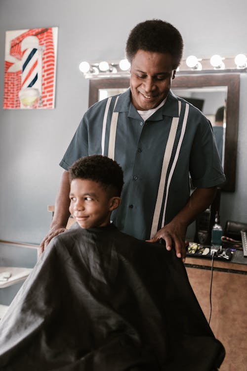 Man in Black and White Polo Shirt Holding Boy on Black Barber Chair