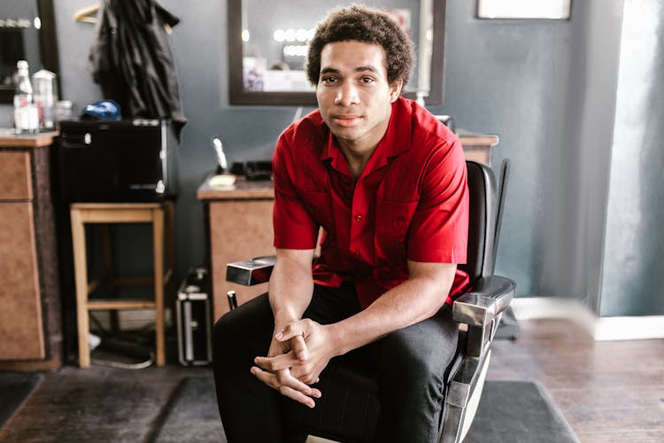 A Man In A Red Shirt Sitting On A Barber Chair