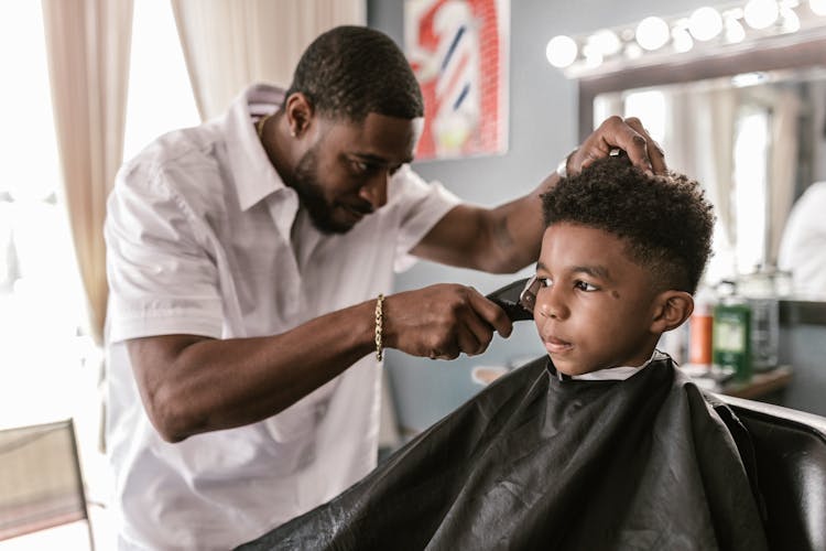 A Barber Holding A Hair Clipper Trimming A Boy's Hair