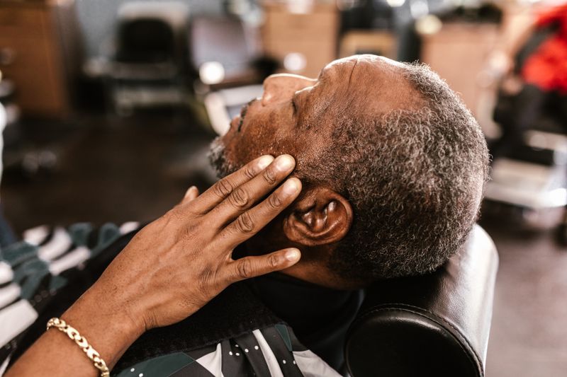 A mature Black man relaxes in a barber chair during a grooming appointment.