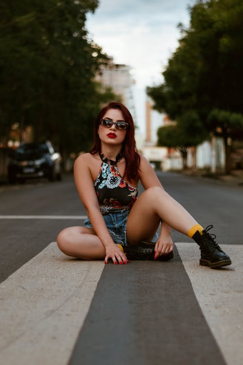 Woman in Sleeveless Top and Denim Shorts Sitting on Road