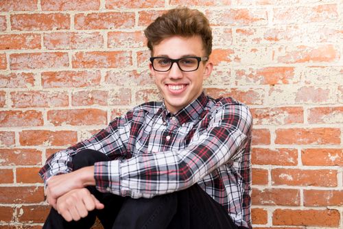 Free Casual portrait of a smiling young man in glasses sitting against a brick wall. Stock Photo
