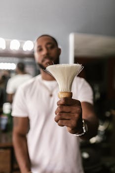 African American barber holding neck duster in focus with blurred background in a barbershop.