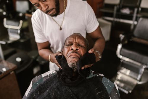 Free Experienced barber providing grooming service using face towel relaxation technique. Stock Photo