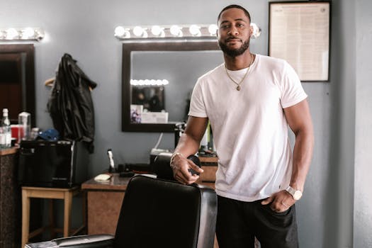 Stylish African American barber stands confidently by a chair in a modern barbershop.