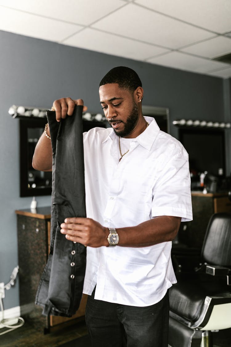 A Man In White Button Down Shirt Folding Black Fabric 