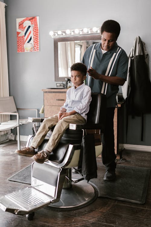 A Man in Striped Shirt Behind a Boy on a Barber Chair
