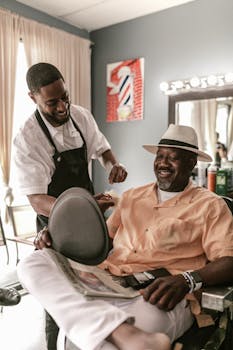 Smiling barber giving a haircut to a cheerful customer in an indoor barber shop setting.