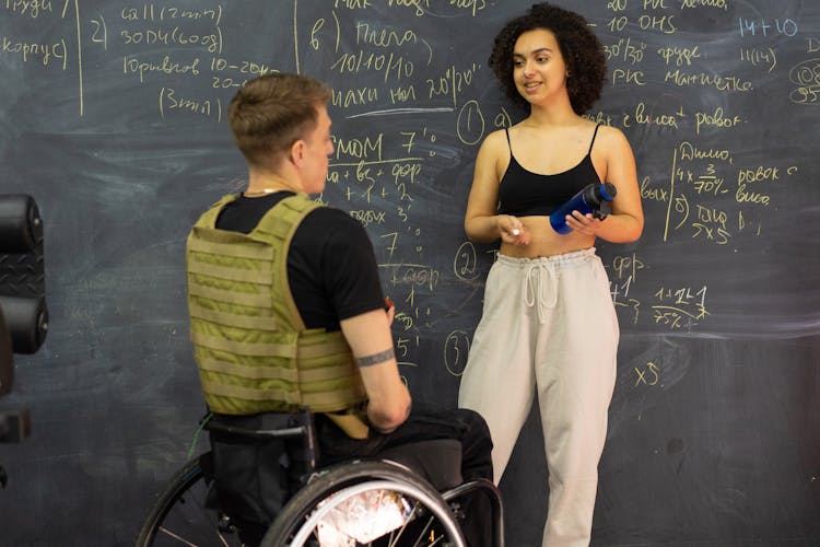 Young Woman Talking With Handicapped Man Near Chalkboard