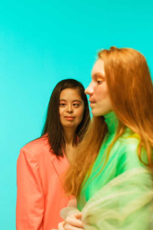 Free Two women wearing vibrant pink and green outfits stand against a bold teal background, exuding fashion and style. Stock Photo