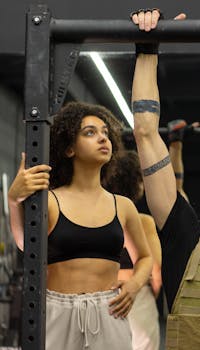 A woman assisting another person during a workout session at the gym, focused and determined.