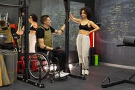 Woman in Black Tank Top and White Pants Standing Beside Black and Red Wheelchair