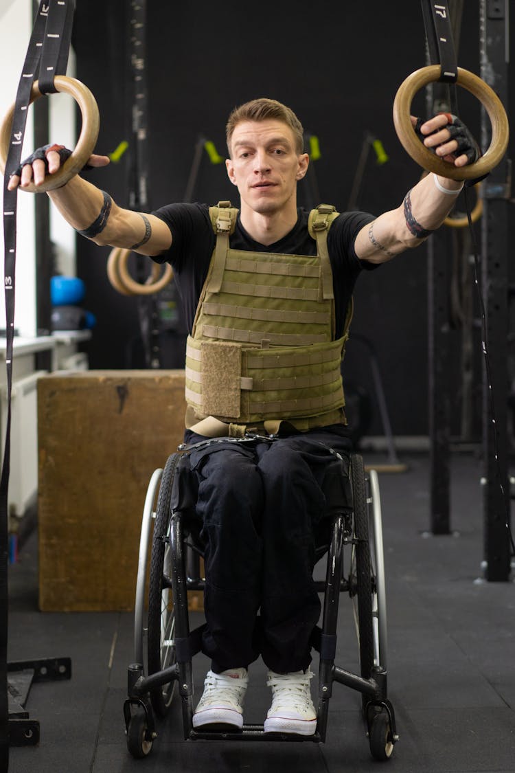 A Man In A Wheelchair Holding A Pull Up Rings